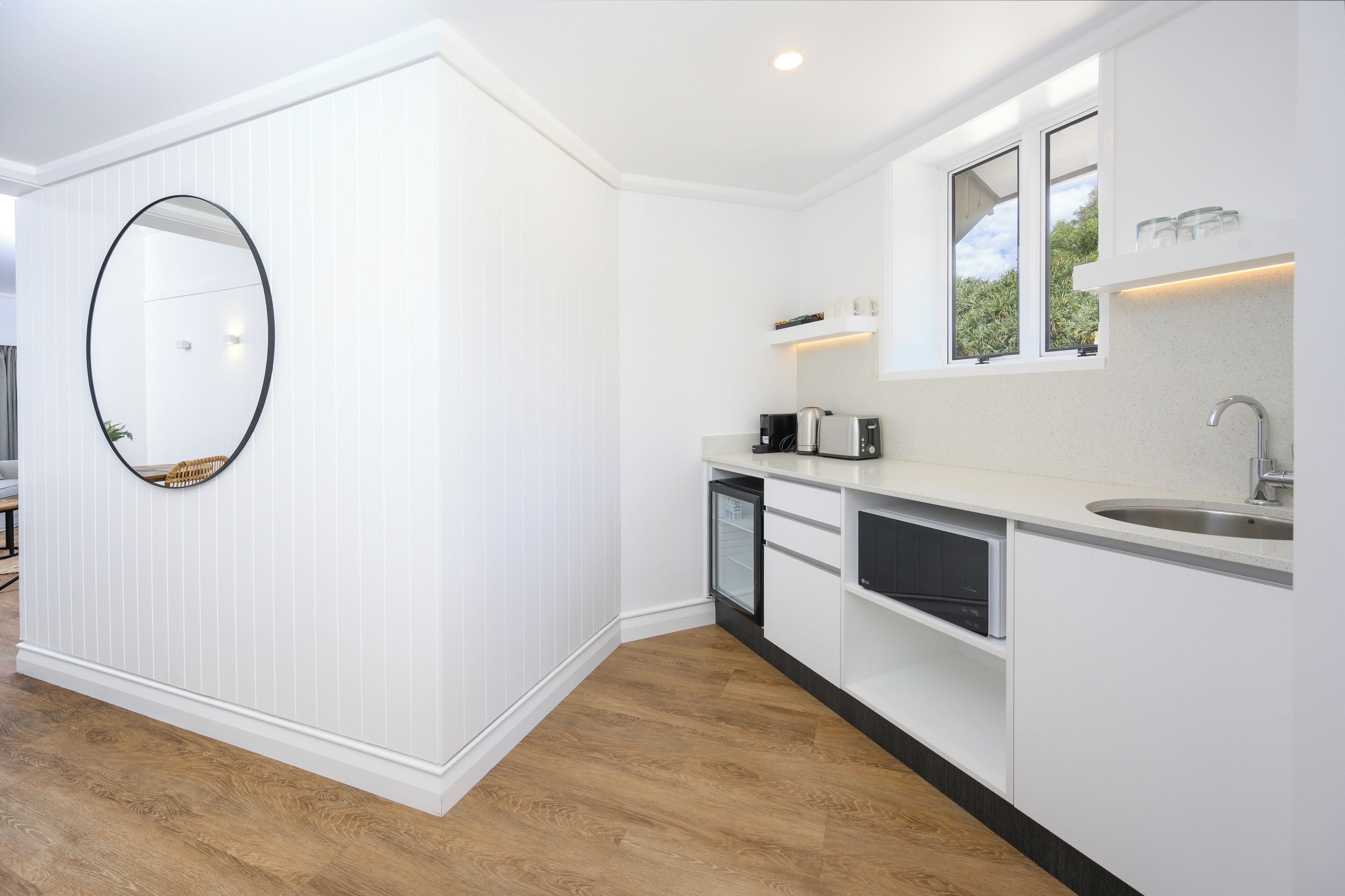 A modern kitchen with white cabinetry, a built-in dishwasher, and a large mirror.