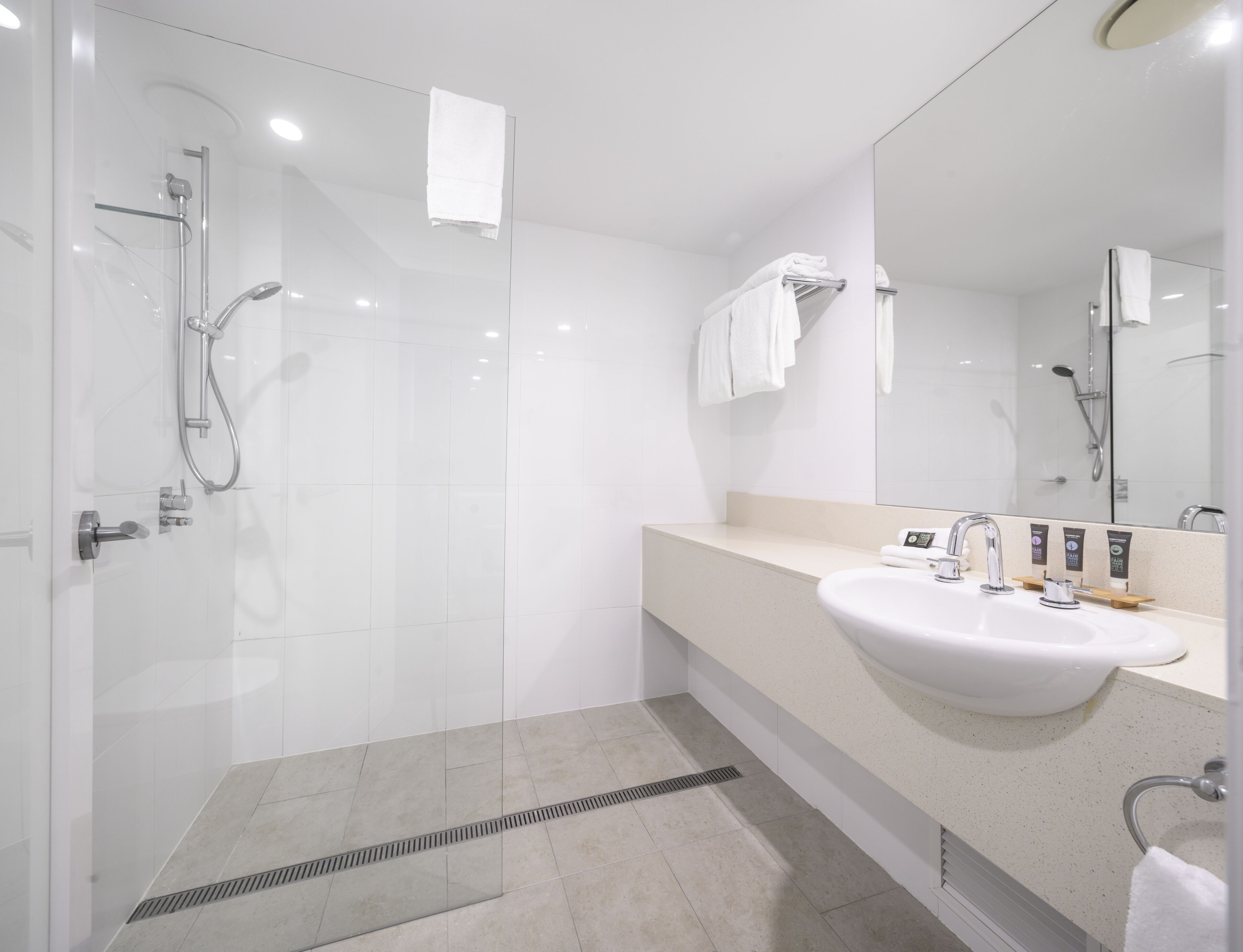 Un baño moderno con ducha de mampara de vidrio, un lavabo blanco y un espejo grande.