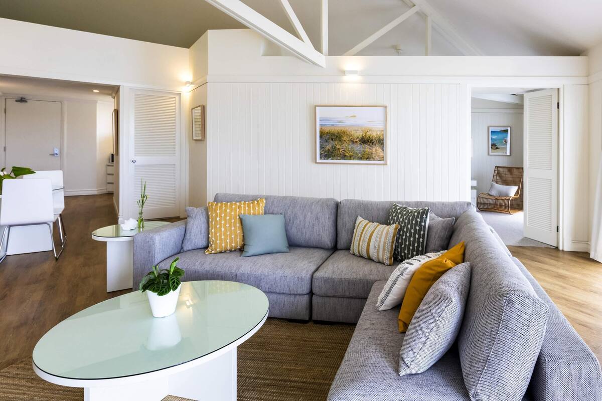 A modern living room with a sectional sofa, a glass coffee table, and a painting on the wall.