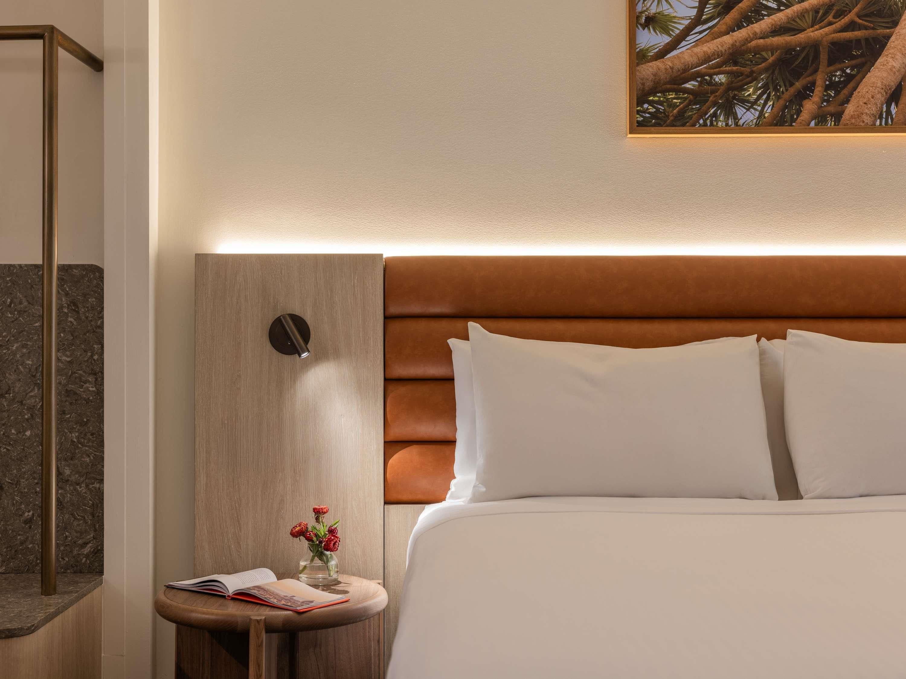 A hotel room with a bed, a nightstand, a reading lamp, and a framed picture on the wall.