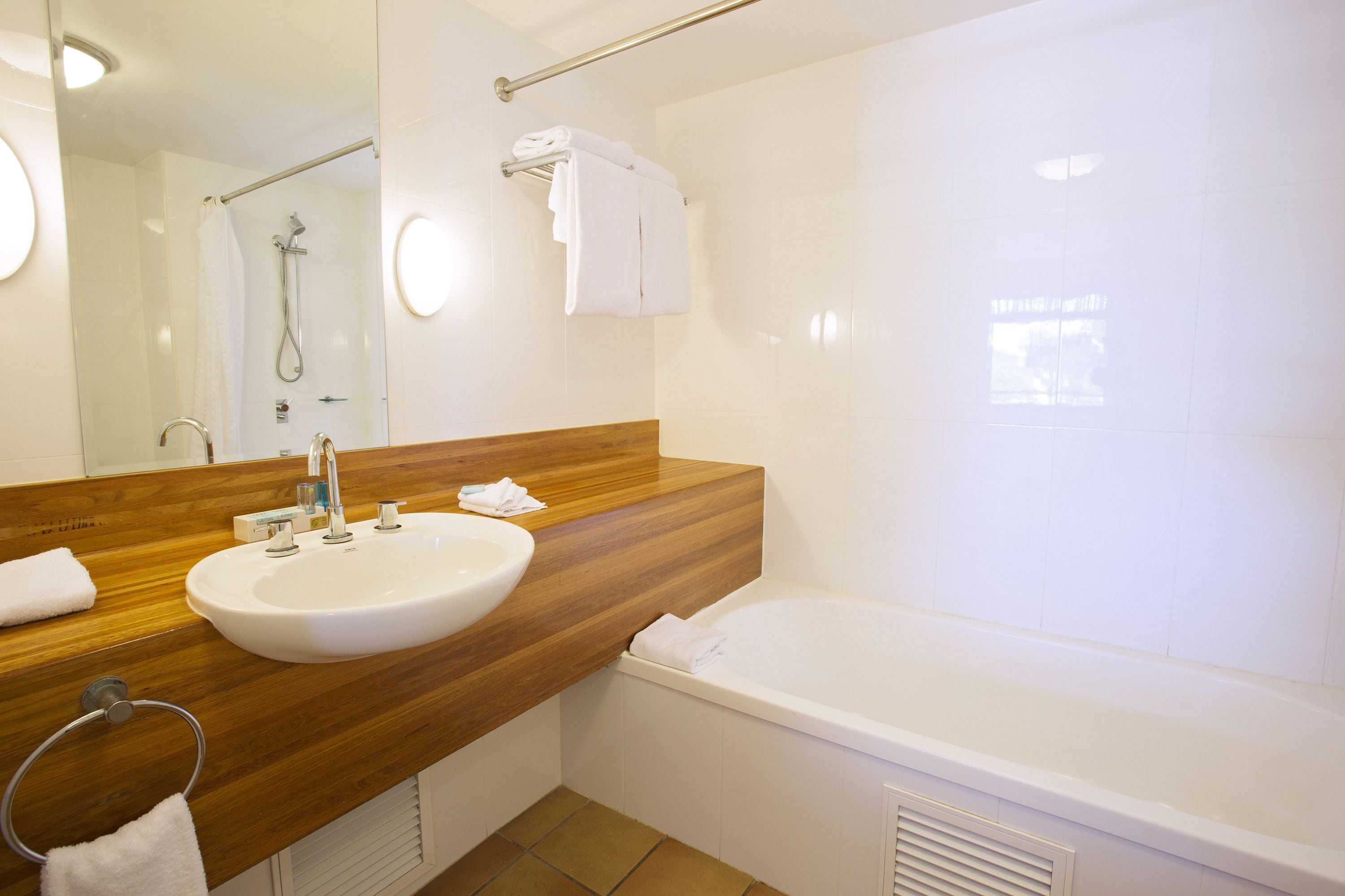 A modern bathroom with a wooden vanity, a white sink, a bathtub, and a shower.
