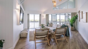 A spacious living area with a large window, a sofa, wicker chairs, and a dining table.