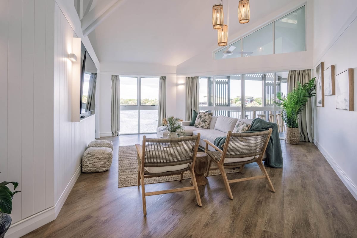 A spacious living area with a large window, a sofa, wicker chairs, and a dining table.