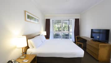 A hotel room with a large bed, a desk with a TV, a chair, and a window with curtains.