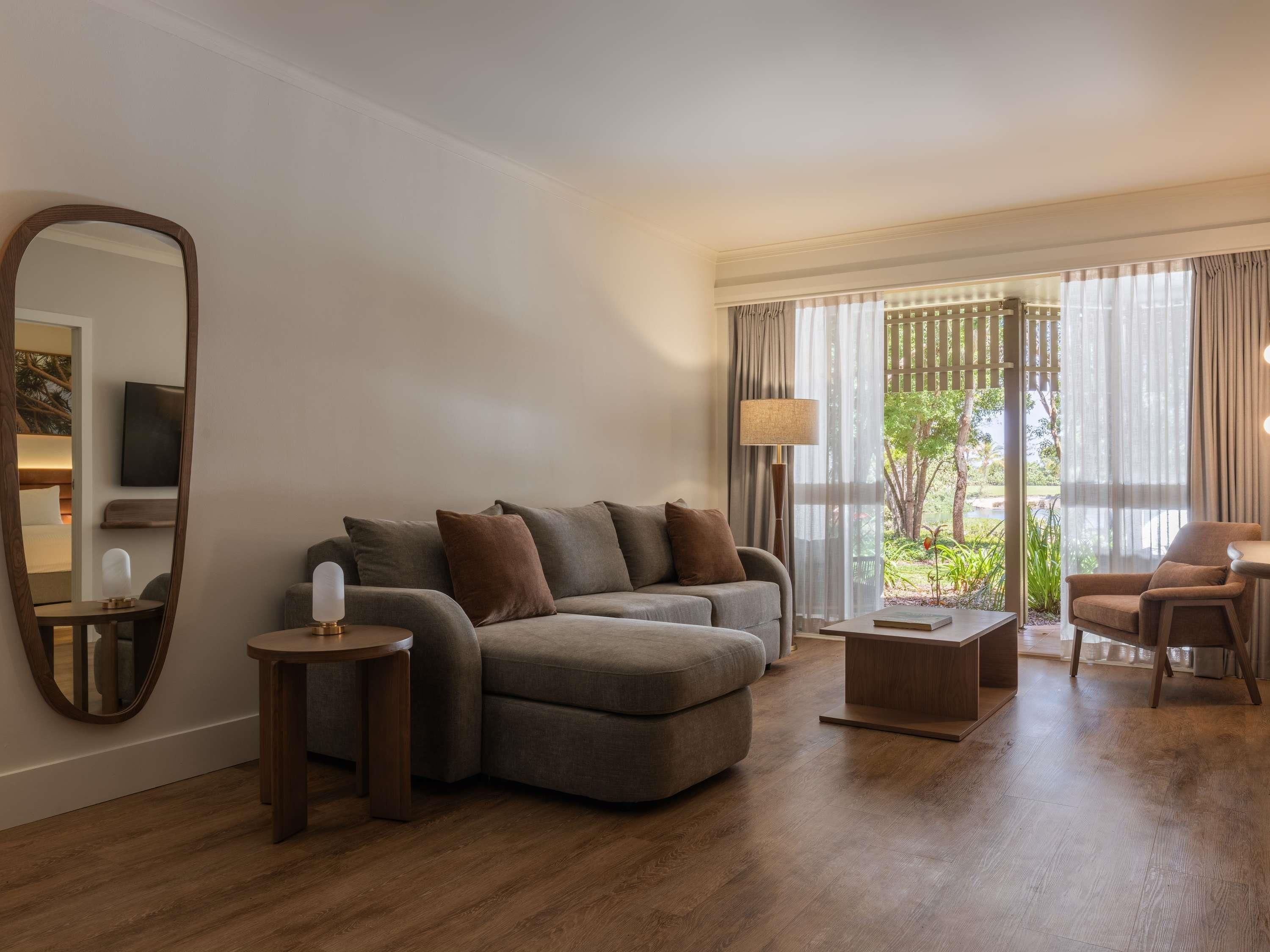 A modern living room with a sectional sofa, a round coffee table, a side table, and a large mirror.