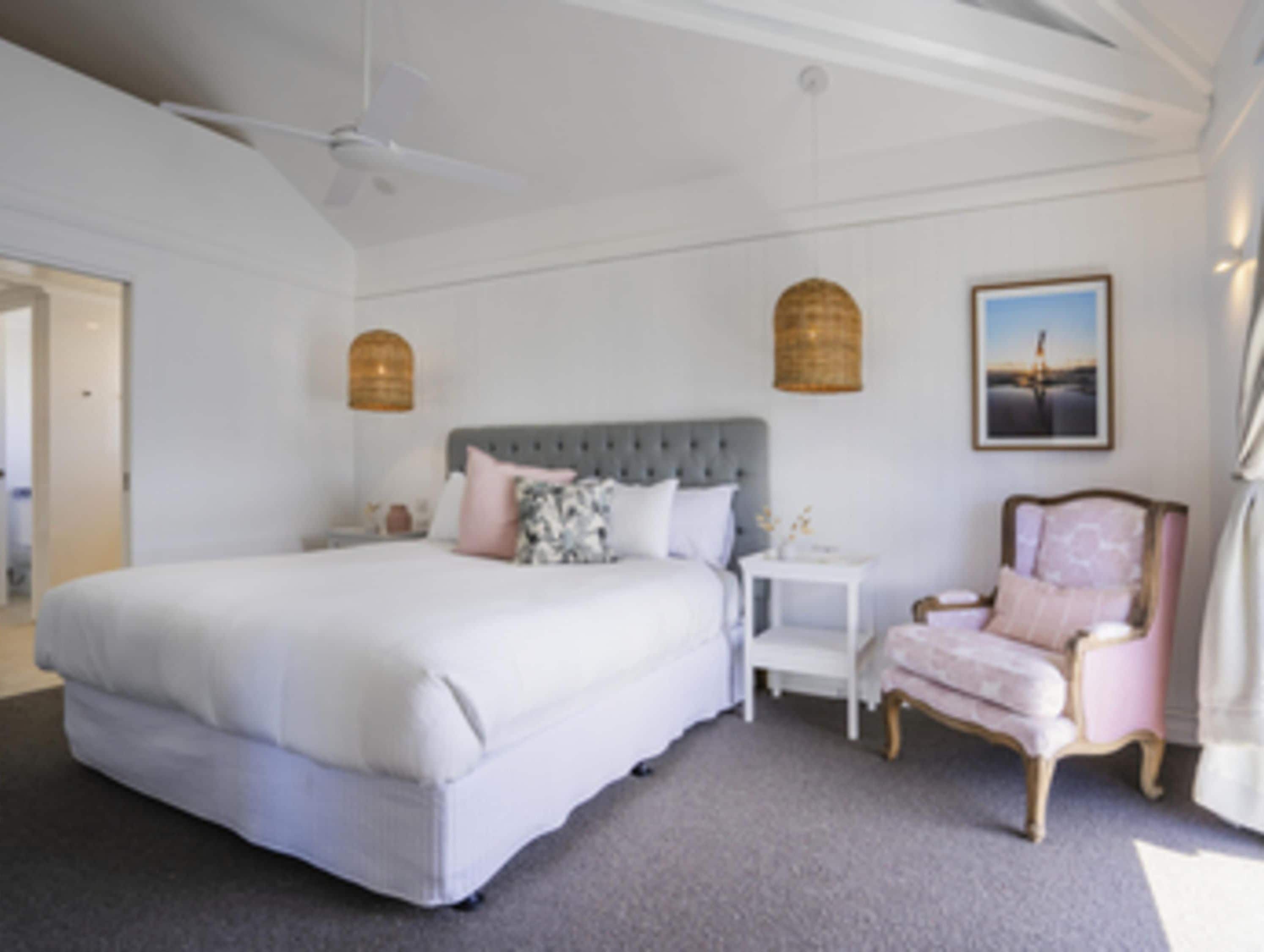 A bedroom with a large bed, a bedside table, a chair, and a wall-mounted light fixture.