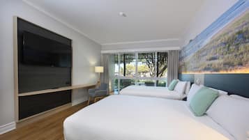 A hotel room with two beds, a flat-screen TV, a chair, a table, and a large window with a view of trees.