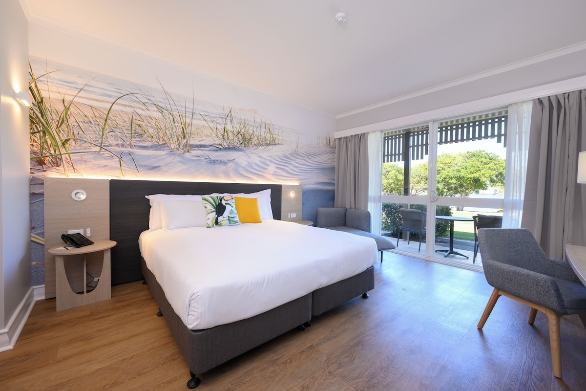 Habitación de hotel moderna con una cama grande, una mesita auxiliar, una silla y vistas al exterior.