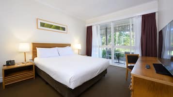 A hotel room with a bed, bedside tables, a desk, a chair, a TV, and a window with curtains.