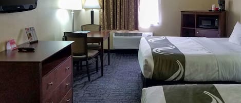 A hotel room with a bed, a desk with a chair, a television, a lamp, a microwave, and a dresser.