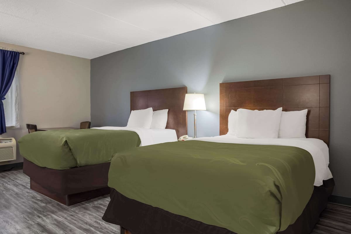 A hotel room with two beds, a desk, a lamp, and a window with curtains.