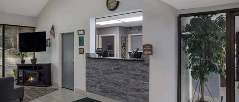 Un hall d’hôtel comprenant un comptoir d’accueil, une cheminée, un téléviseur et une grande plante en pot.