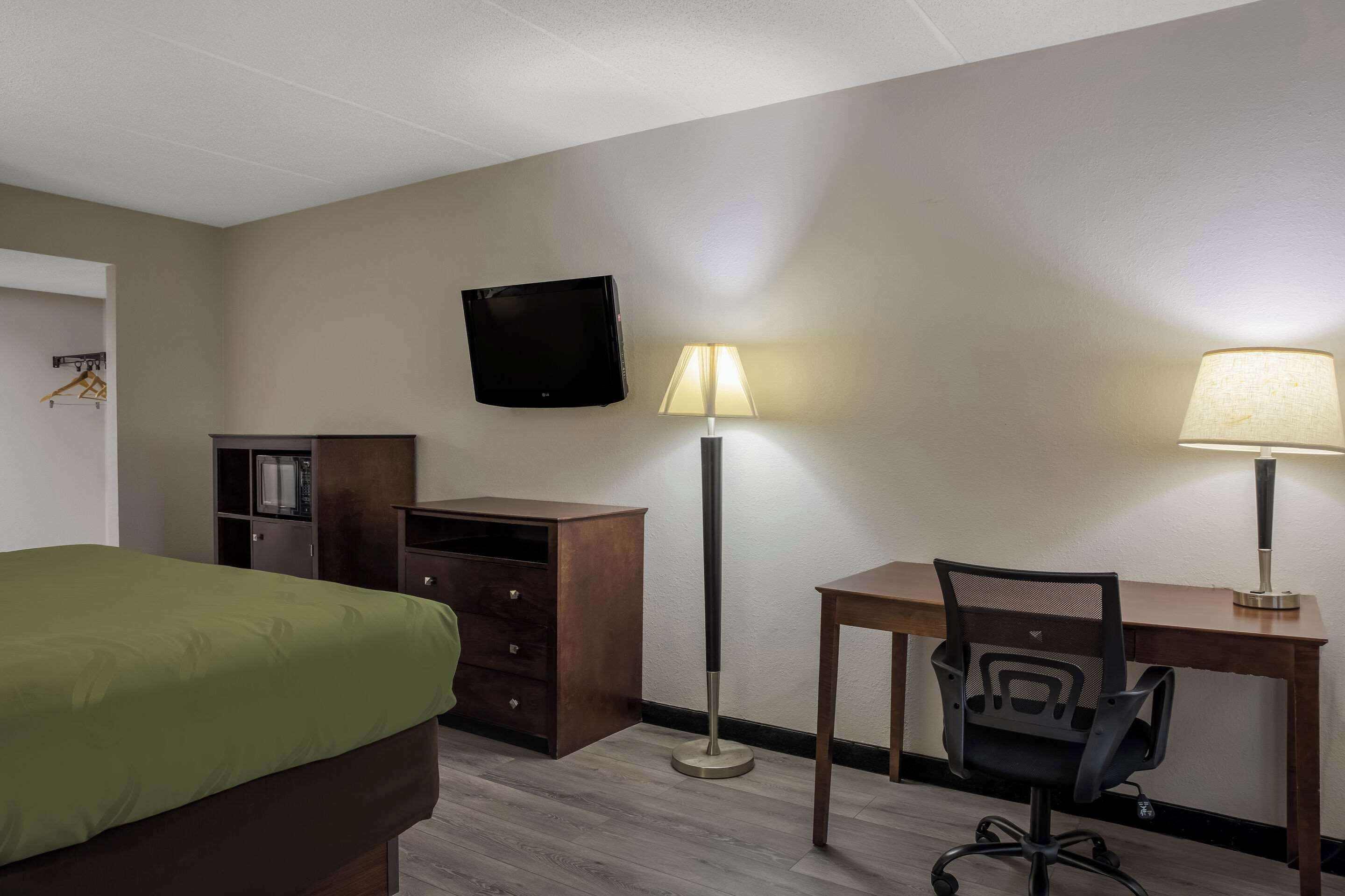 Une chambre d’hôtel équipée d’un lit, d’un bureau, d’une chaise, d’une télévision et de deux lampadaires.
