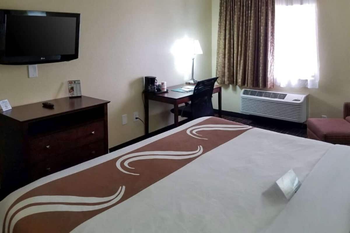 A hotel room with a bed, a desk, a television, a lamp, and an air conditioning unit.