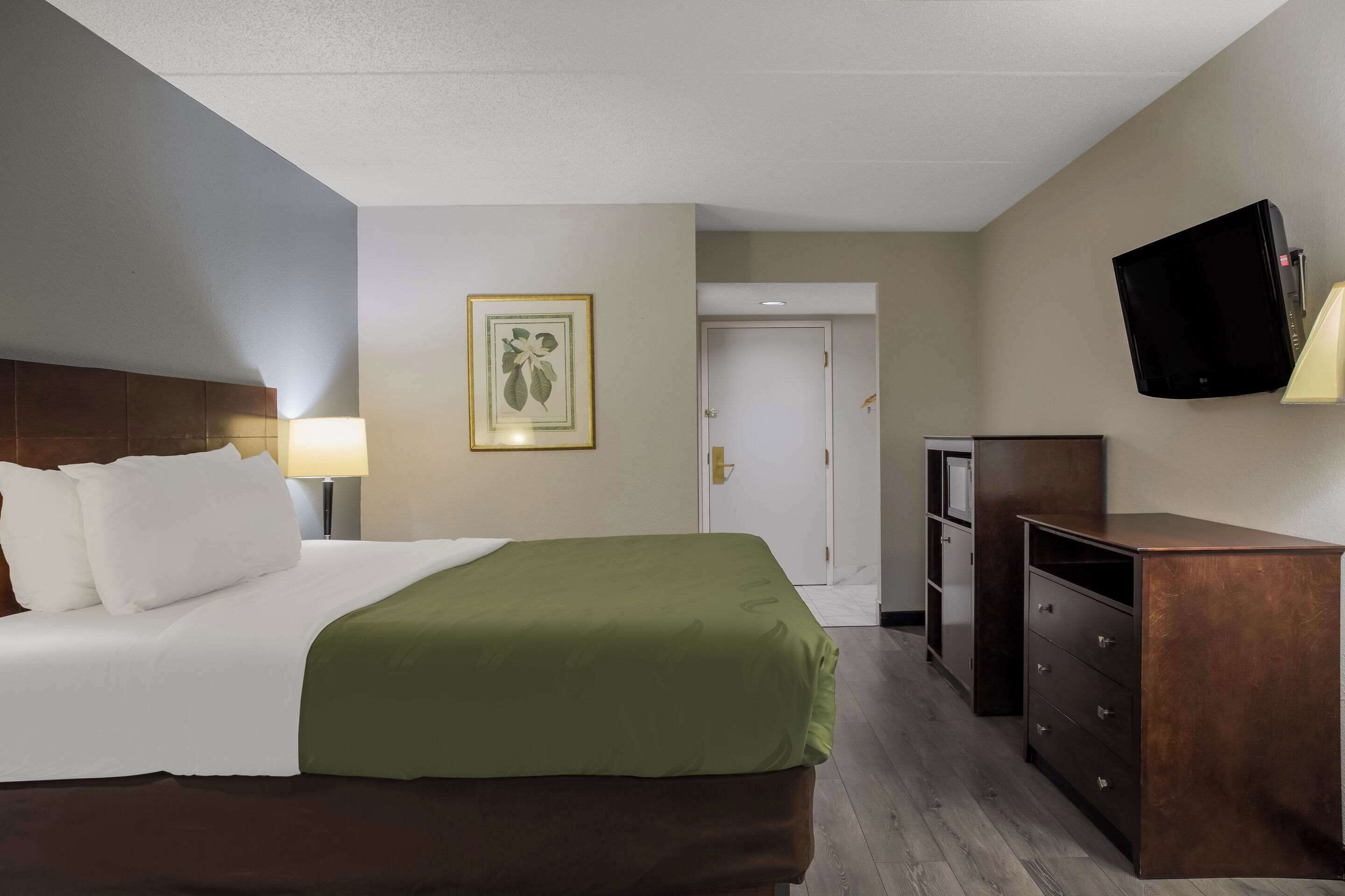 A hotel room with a bed, a desk, a television, and a door.