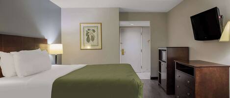A hotel room with a bed, a desk, a television, and a door.