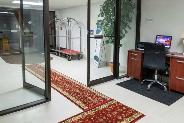 A modern office space with a desk, chair, computer, and a red carpet leading to a glass door. - Quality Inn Toledo Westgate (Toledo)