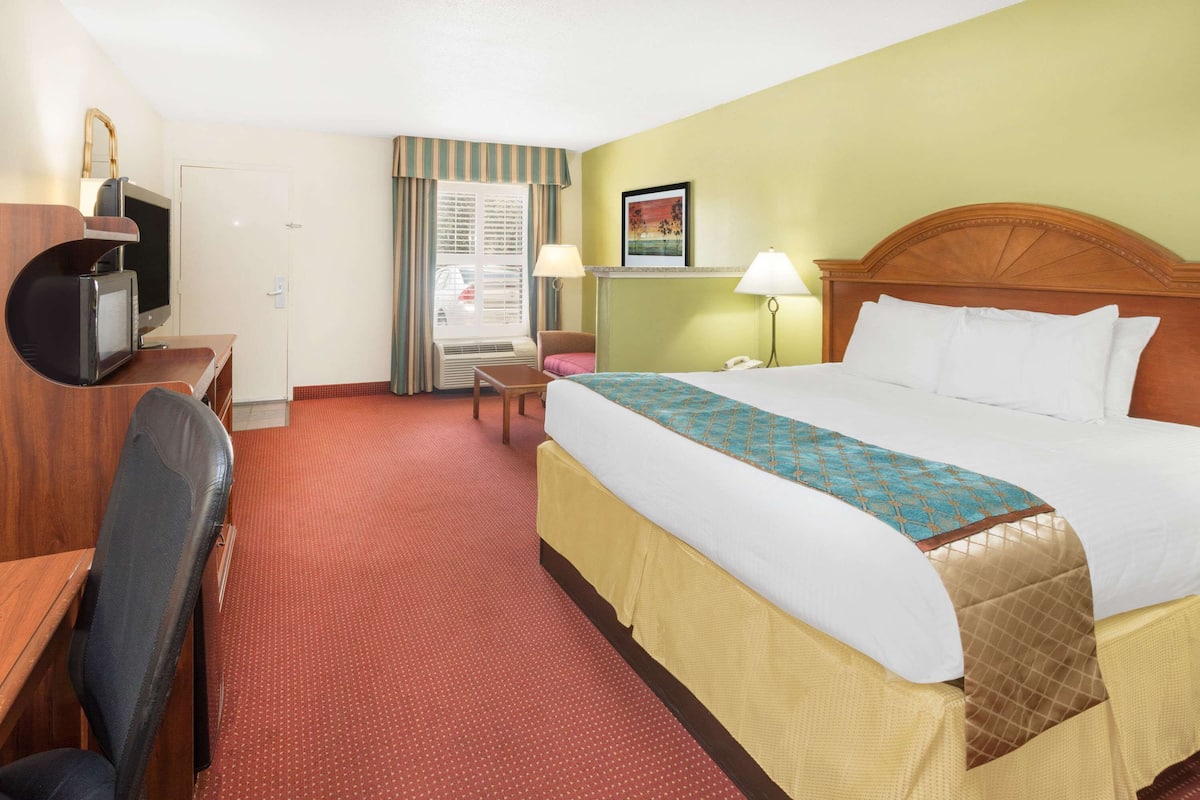 A hotel room with a bed, a desk with a computer, a chair, a television, and a window with curtains.