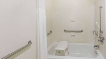 A bathroom with a bathtub, a shower, and a handrail.