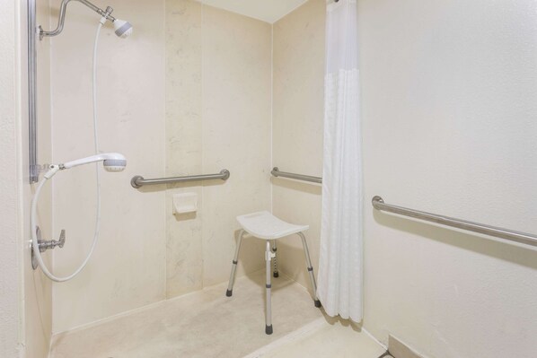 A wheelchair-accessible shower area with a handheld showerhead, grab bars, and a white shower seat. - Baymont by Wyndham Orangeburg North (Orangeburg)