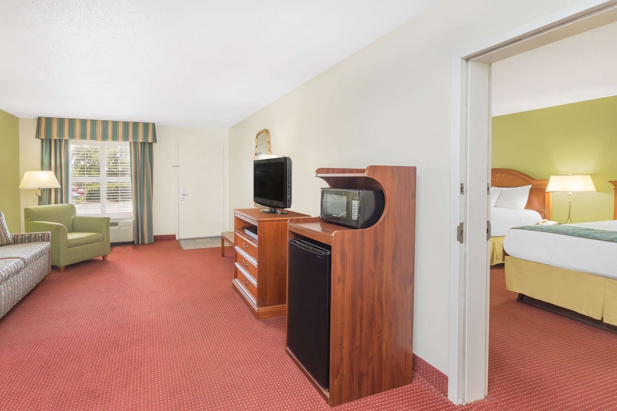 A hotel room with a bed, a desk with a television and microwave, a chair, and a dresser.