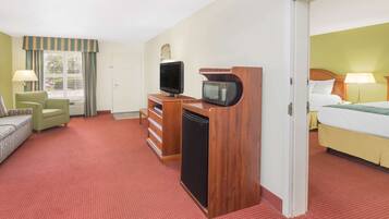 Habitación de hotel con cama, escritorio con televisión y microondas, una silla y cómoda.
