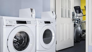 A laundry room with two Whirlpool commercial duty washers, a door, and an exercise machine in the background. - Days Inn by Wyndham Jamestown (Jamestown)