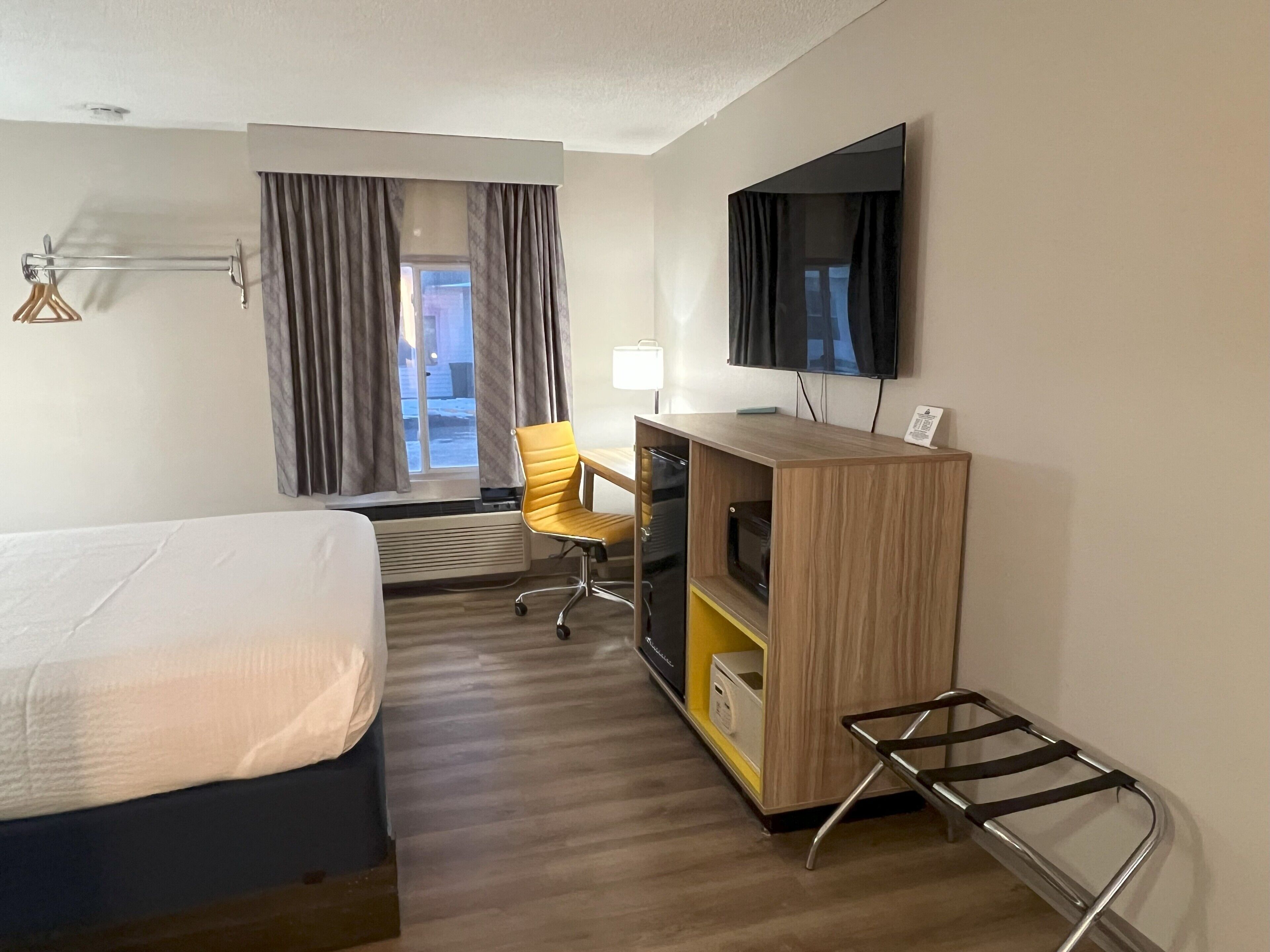 A hotel room with a bed, a desk, a chair, a TV, and a window with curtains.