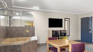 A modern hotel room with a bathtub, a wooden table, purple chairs, a flat-screen TV, and a blue door. - Days Inn by Wyndham Jamestown (Jamestown)