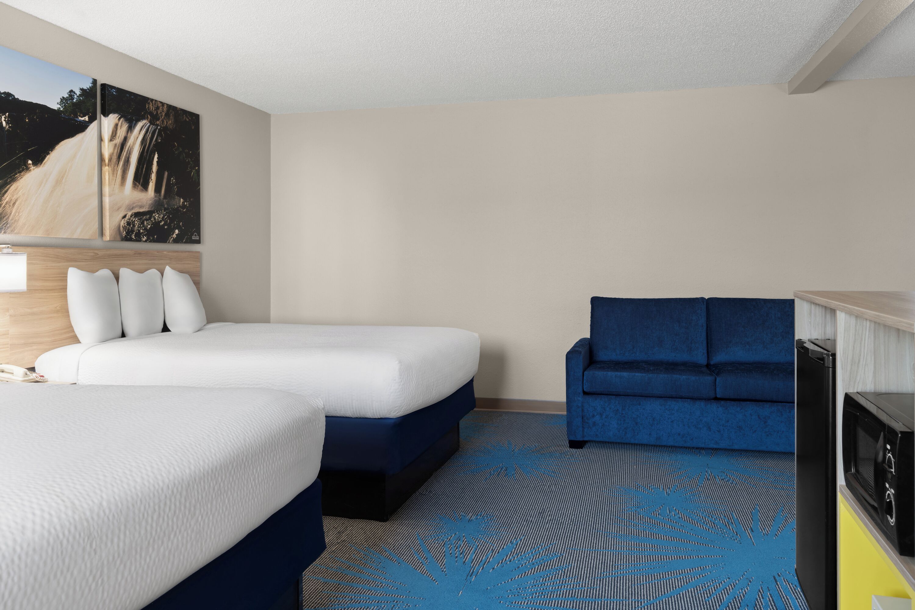 A hotel room with a large bed, a blue sofa, a TV, and a painting of a waterfall.