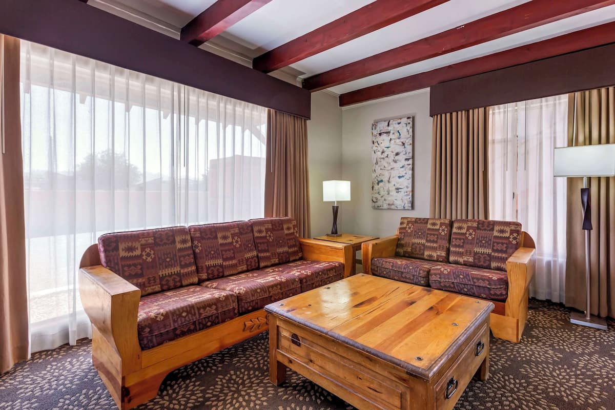 A cozy living room with a wooden sofa and armchair, a wooden coffee table, and a patterned rug.