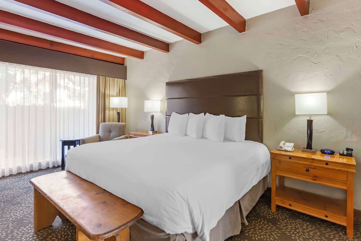 A hotel room with a large bed, a wooden nightstand, a bench, and a desk with a lamp.