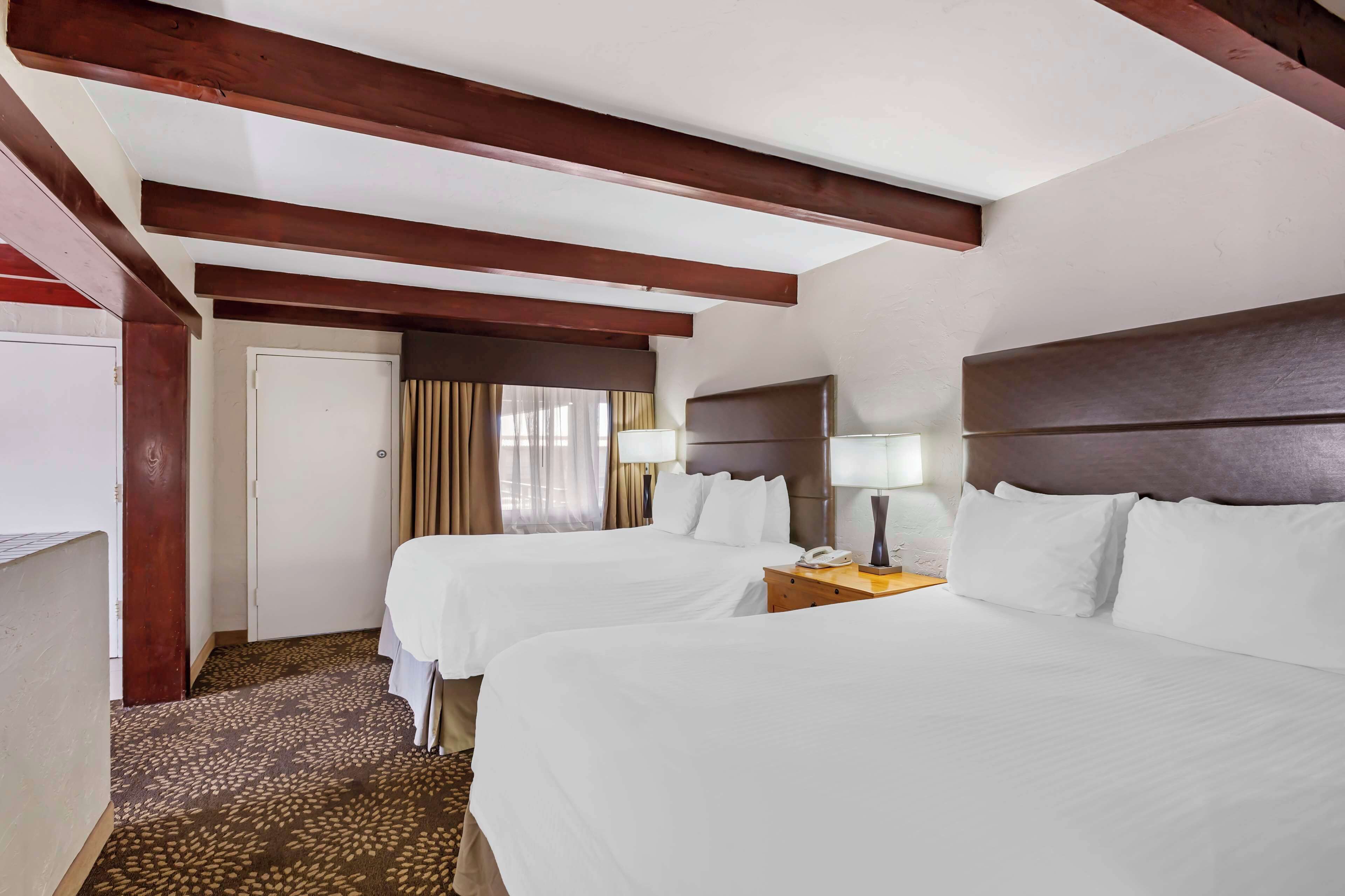 Habitación de hotel con dos camas, vigas de madera en el techo, una puerta y una ventana con cortinas.