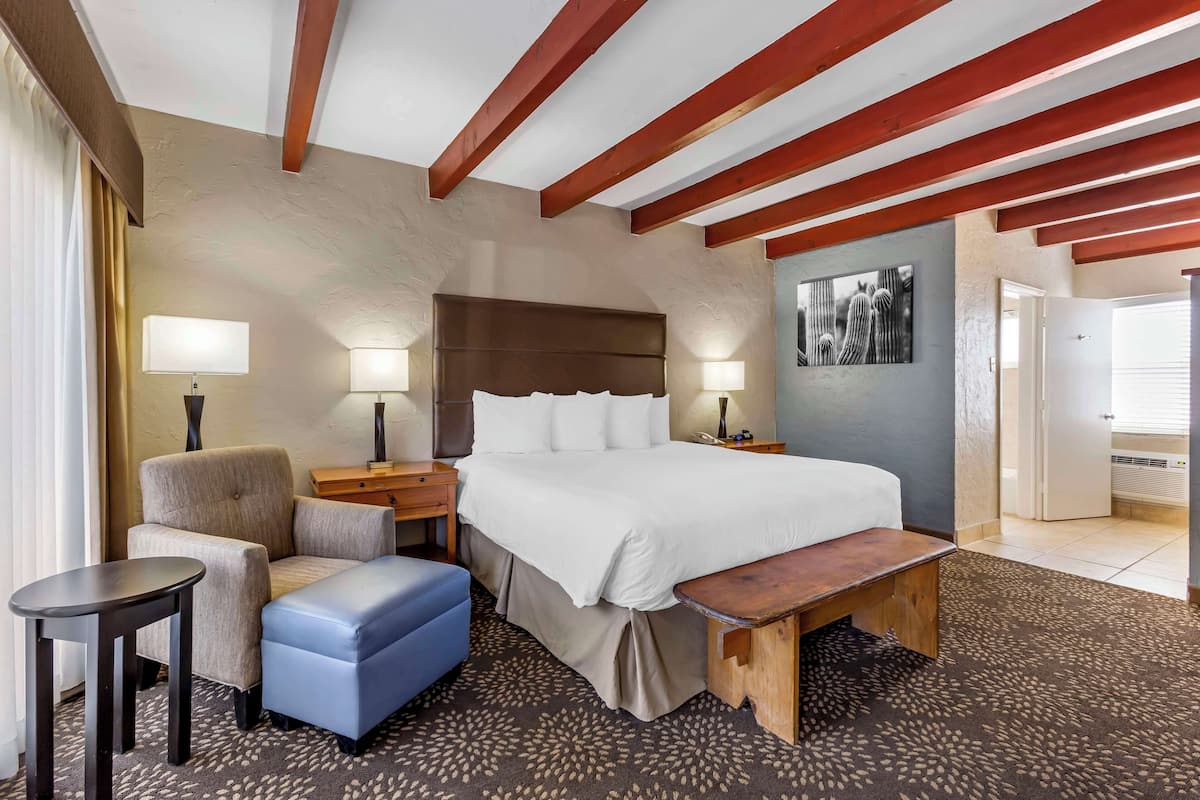 A hotel room with a large bed, a desk, a chair, a bench, and a small table.