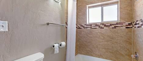 A bathroom with a toilet, a shower with a curtain, a bathtub, and a window.
