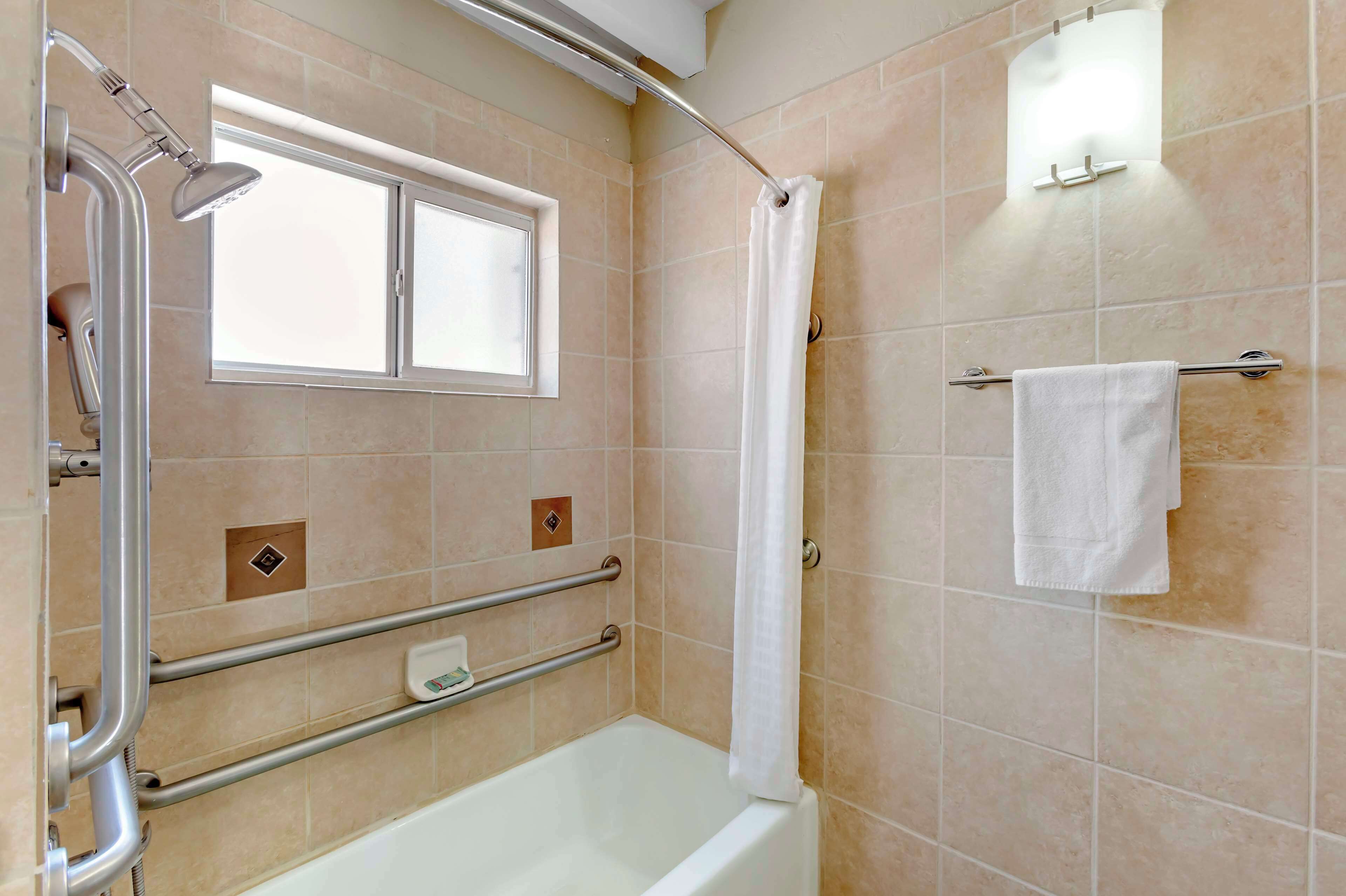 A bathroom with a bathtub, a shower, a window, and a towel rack.