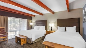 A hotel room with two beds, wooden benches, a desk, and a chair.