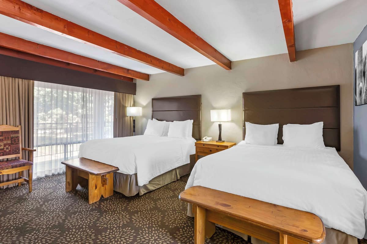 A hotel room with two beds, wooden benches, a desk, and a chair.