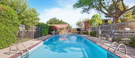 A rectangular swimming pool with metal railings, surrounded by a brick deck and metal fence.