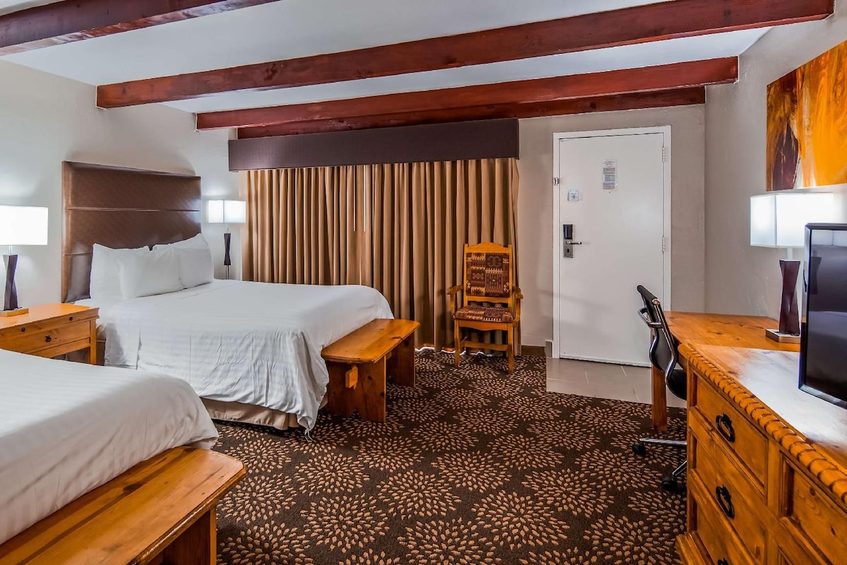 A hotel room with two beds, a wooden bench, a desk, a chair, a television, and a door.