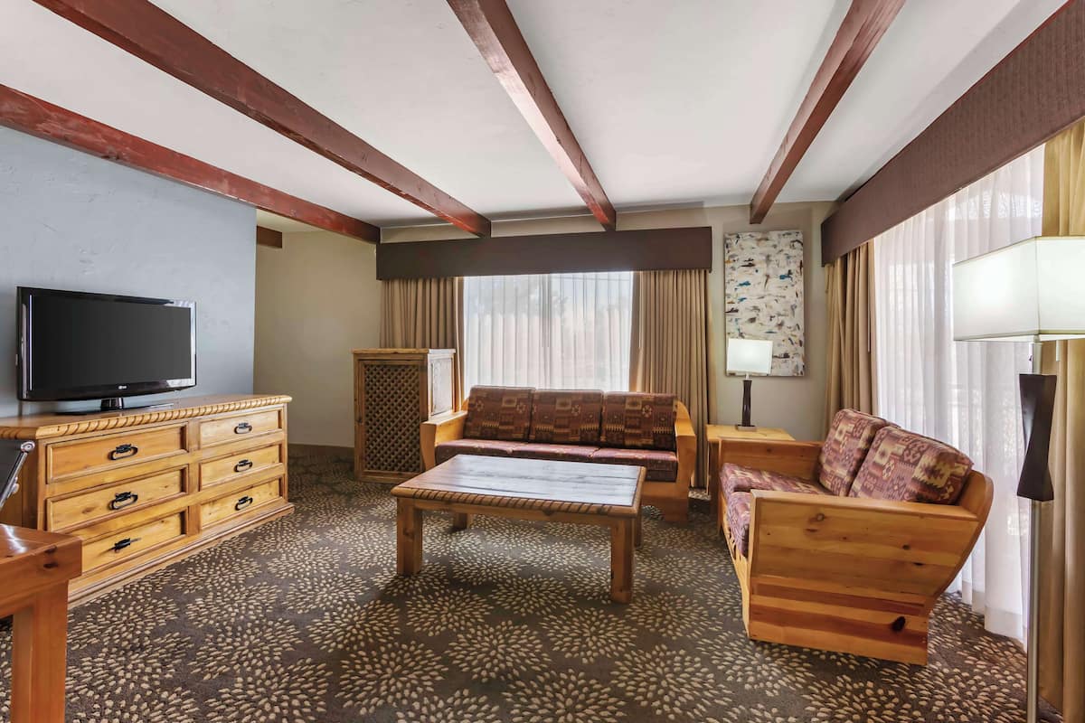 A room with a wooden sofa, a wooden coffee table, a TV on a wooden cabinet, and a patterned carpet.