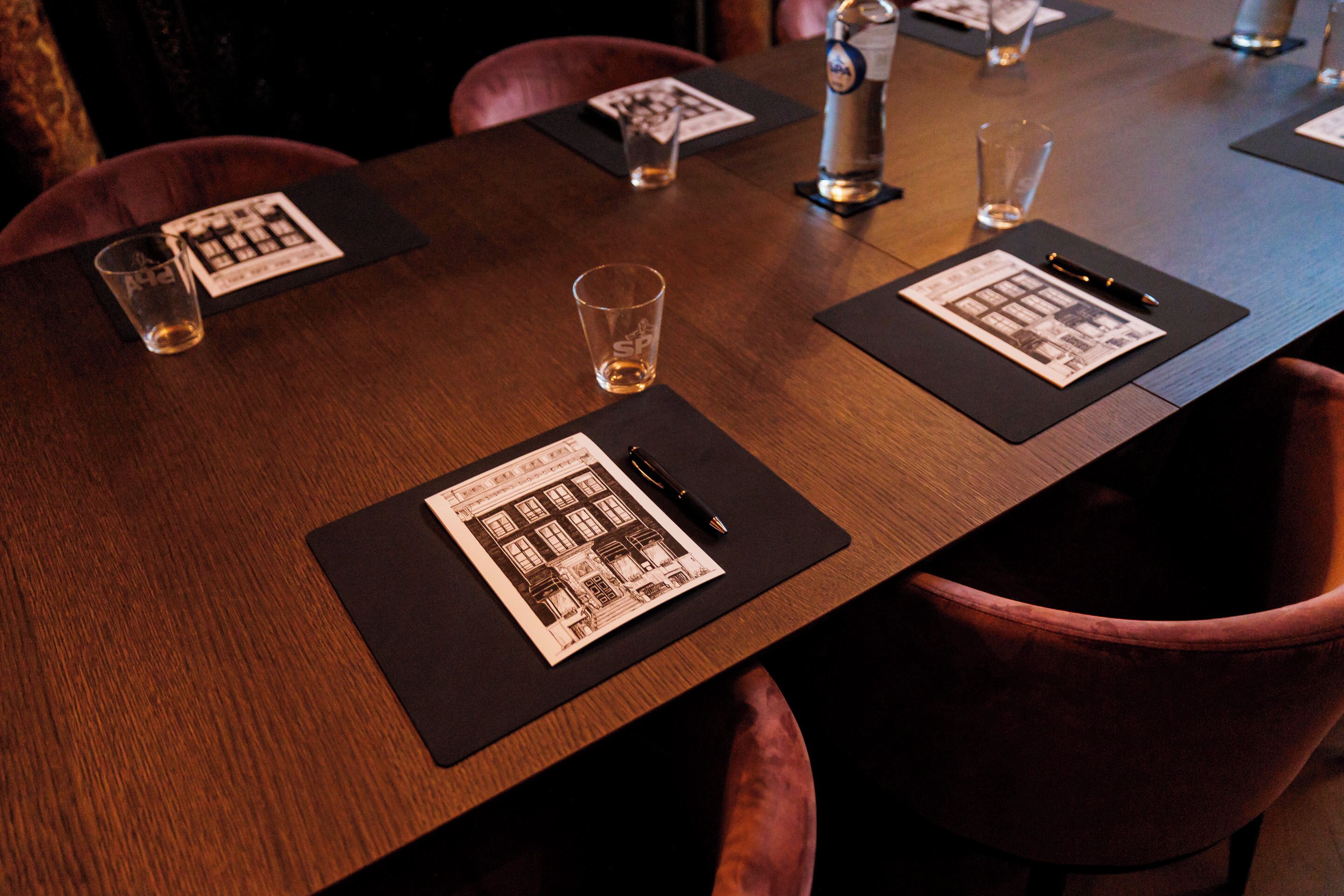 A conference table with black placemats, glasses, and a pen.