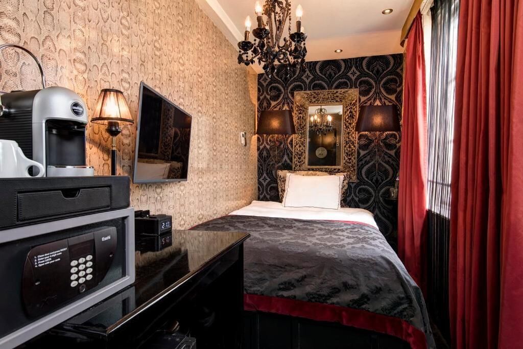 A hotel room with a bed, a TV, a coffee machine, a desk with a computer, and a mirror.
