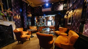 A bar area with orange upholstered chairs, a marble fireplace, and a chandelier.