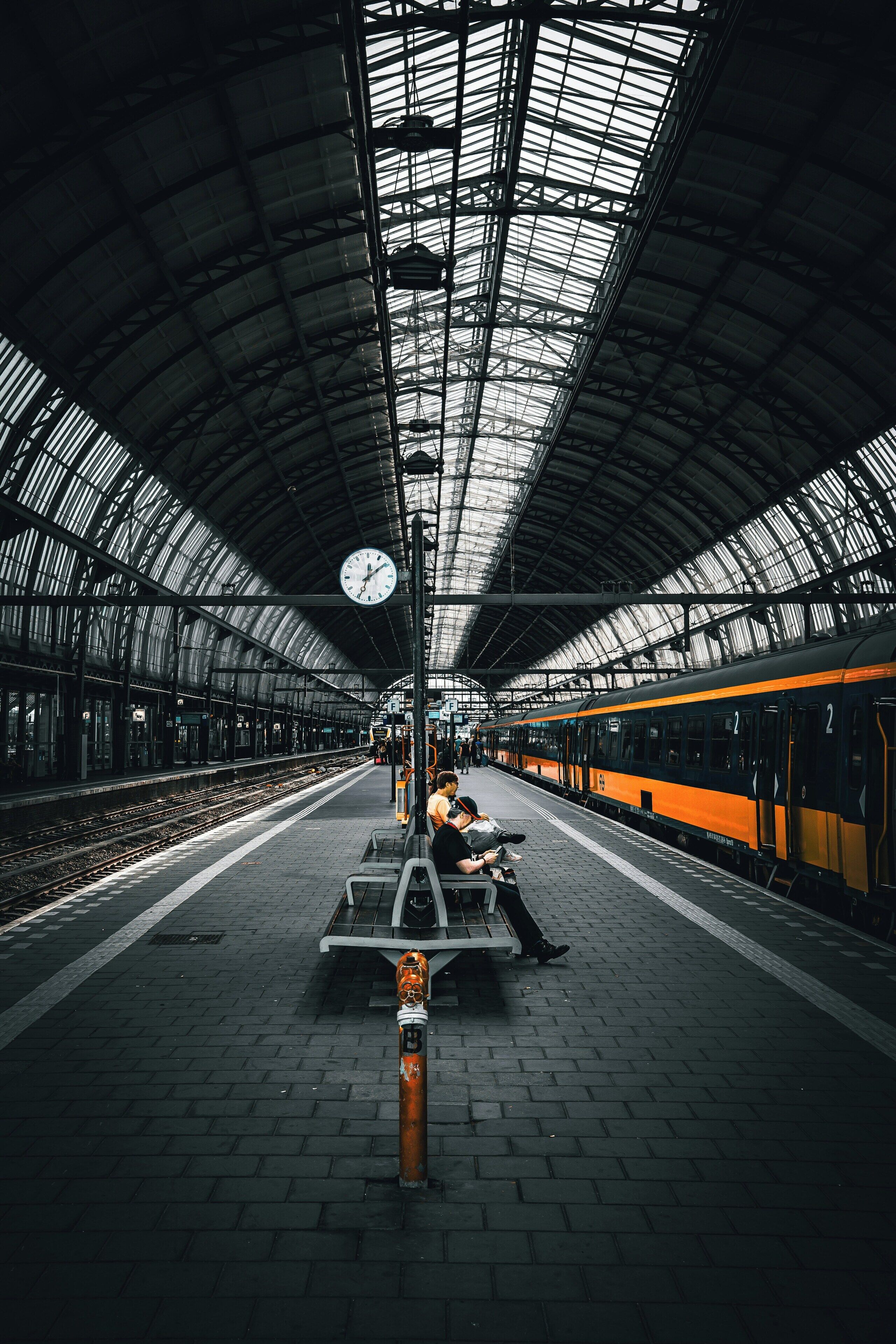 Andén de estación de tren con techo curvo, bancos y un reloj.
