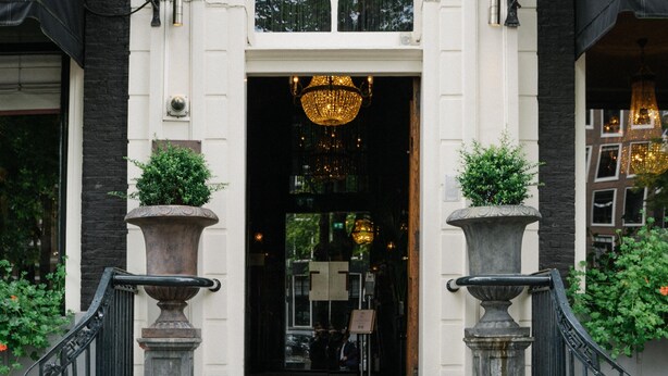 A building entrance with a grand staircase, two large planters, and a chandelier.