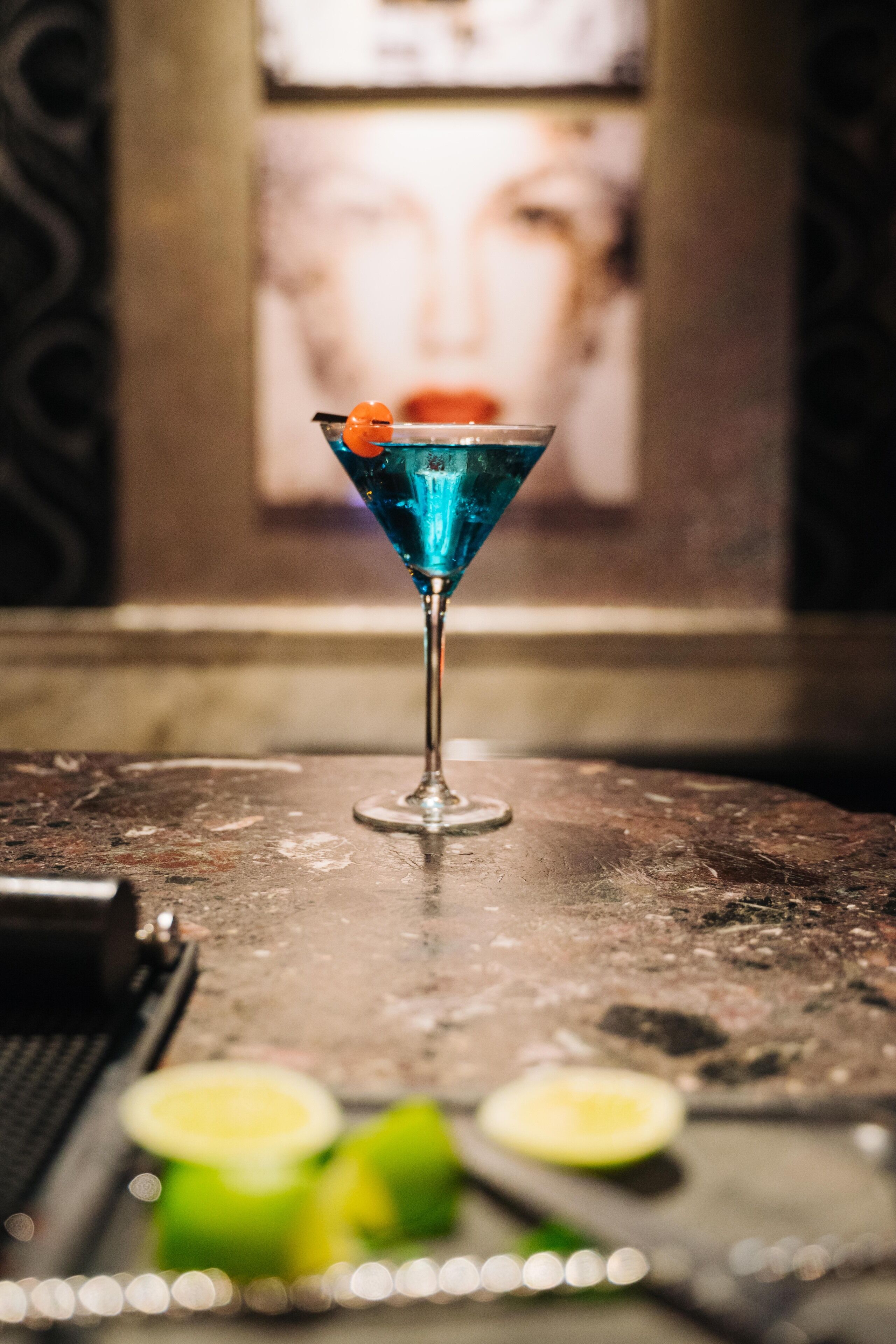 Una copa de martini con un líquido azul y una guarnición de naranja sobre una mesa.