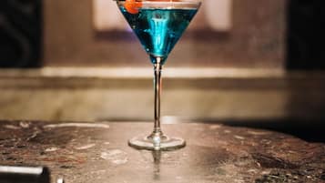 Una copa de martini con un líquido azul y una guarnición de naranja sobre una mesa.