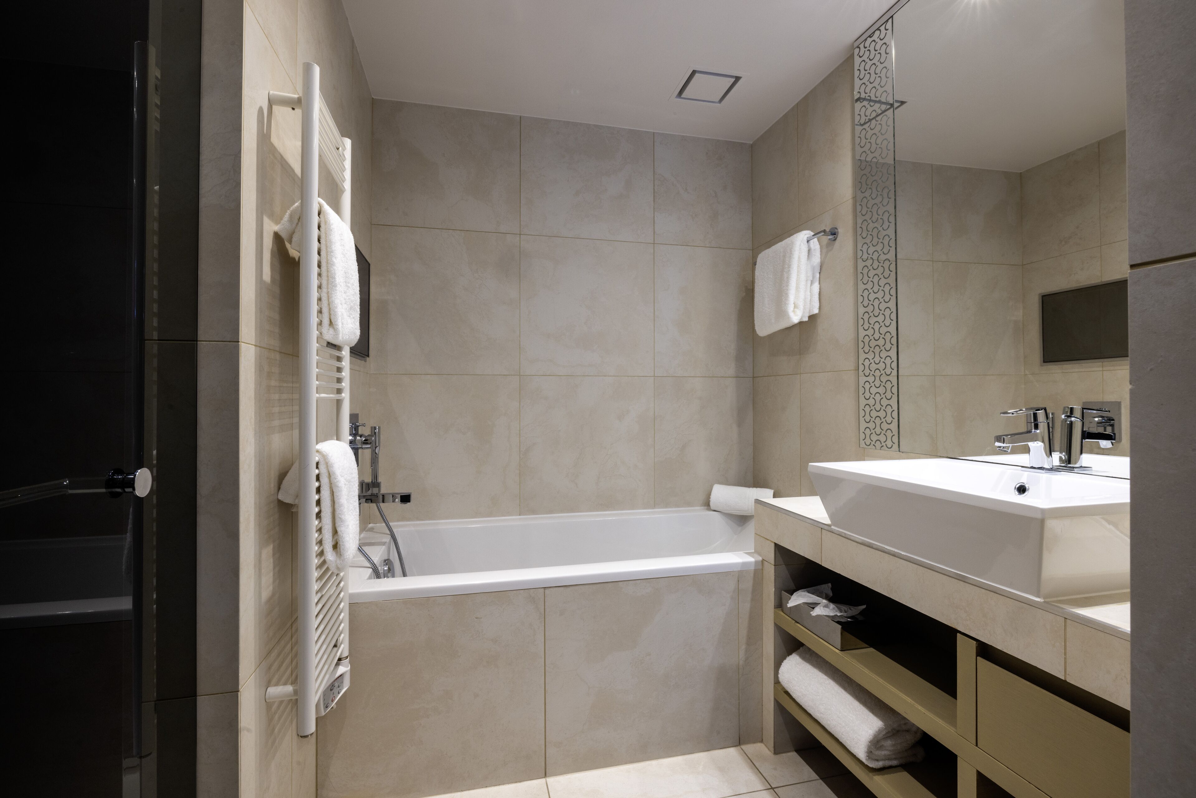 Une salle de bain moderne avec une baignoire, un grand miroir, un lavabo et un porte-serviettes.