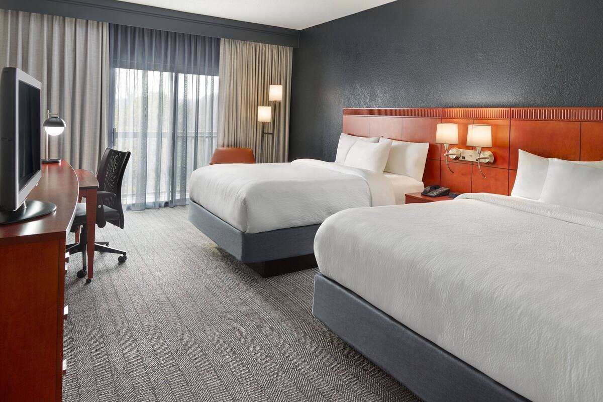 A hotel room with two beds, a desk with a TV, and a chair.